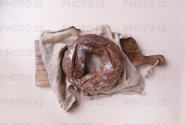 Round handmade rye bread on wooden board with linen napkin, on beige background top view, copy