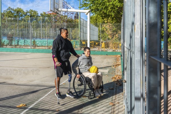 Friends celebrating sports inclusion on a sunny outdoor basketball court, one man with crutches and