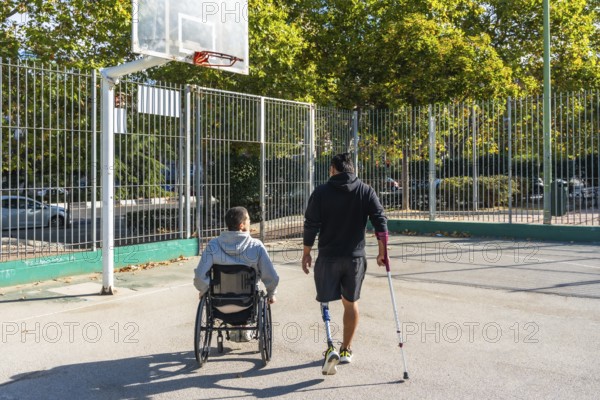 Two young men, one in a wheelchair and the other with a prosthetic leg, are walking together