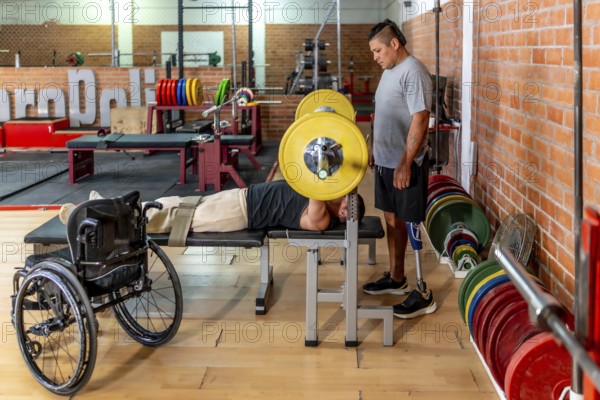 Two determined men training in a gymone bench pressing weights while his teammate with a prosthetic