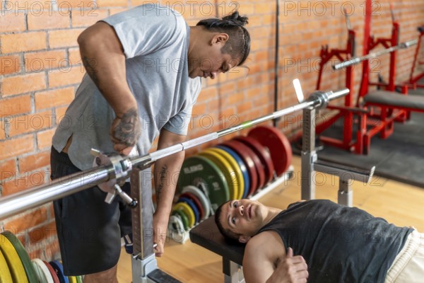 Two men in a gym, adaptive athlete bench pressing while a personal trainer spots and adjusts the