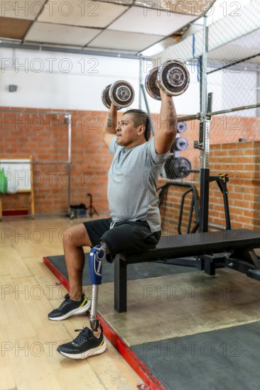 Man with a prosthetic leg performing overhead dumbbell presses while sitting on a weight bench,