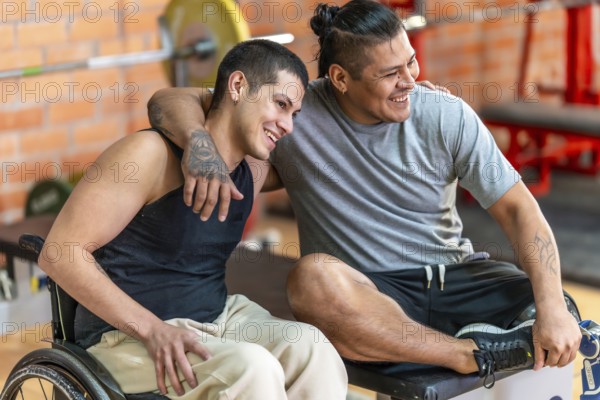 Two diverse adult men with disabilities smiling and embracing, one in a wheelchair and the other