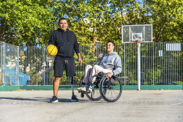 Two young men, one with a prosthetic leg holding a basketball and another sitting in a wheelchair,