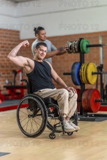Adaptive athlete in a wheelchair flexing his bicep and smiling while a trainer adjusts weight