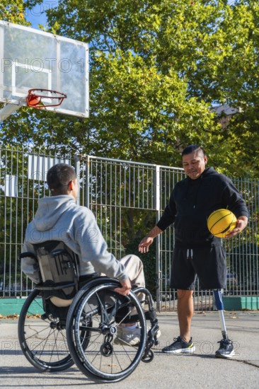Two disabled men are enjoying a game of basketball on an outdoor court, with one man using a