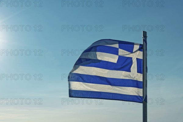 The Greek flag flies in the wind against a clear blue sky with sunshine, Church of the Virgin Mary
