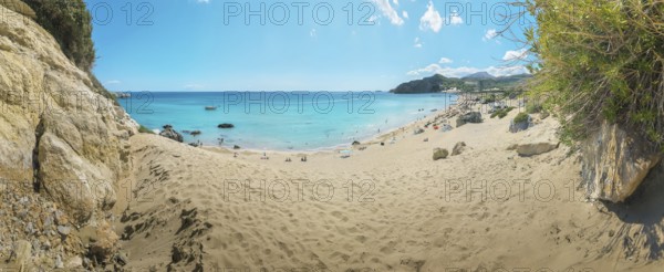 A quiet place on Tsambika sandy beach of Tsambika with clear blue sea and rocks under a sunny sky,