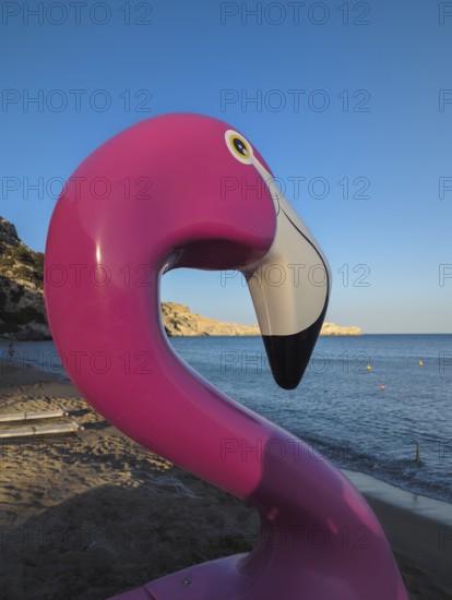 Pink flamingo pedal boat on Tsambika sandy beach with sea in the background at sunset, Tsambika