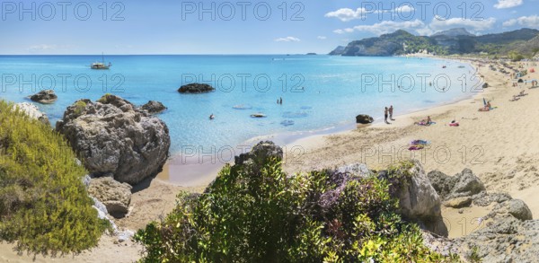 Picturesque Tsambika bay with clear water, rocks and sandy beach. People enjoying the sun, a boat