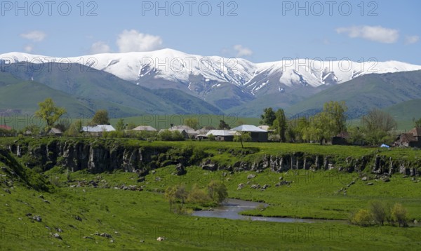 A village in a green landscape with snow-capped mountains in the background, Saratovka, Lesser