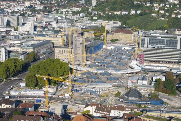 Urban construction project with glass structures and cranes, embedded in a green urban backdrop,