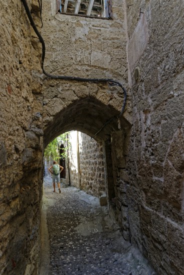 Cobbled alley with arched passageway and stone walls, a man in the background, Medieval town of