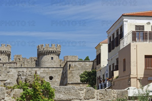Castle with medieval stone towers next to a Mediterranean building under a blue sky, Grand Master's