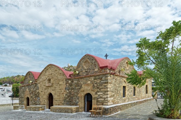 Small stone church Kimisis tis Theotokou with red roofs, surrounded by trees under a clear blue