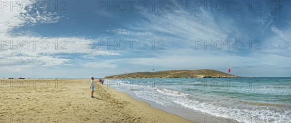 Wide sandy beach of Prasonisi with gentle waves, distant peninsula and kite surfers under a blue