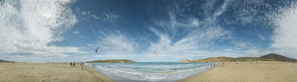 Beach panorama of Prasonisi with light sand, blue sea and two kite surfers under a cloudy sky,