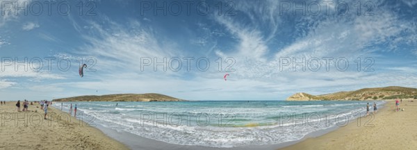 Spacious beach of Prasonisi with light sand, blue sea and two kite surfers under a cloudy sky,