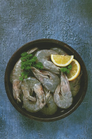 Fresh raw white-footed shrimp, tiger prawns vannamey, on a clay plate, with lemon and herbs, on a