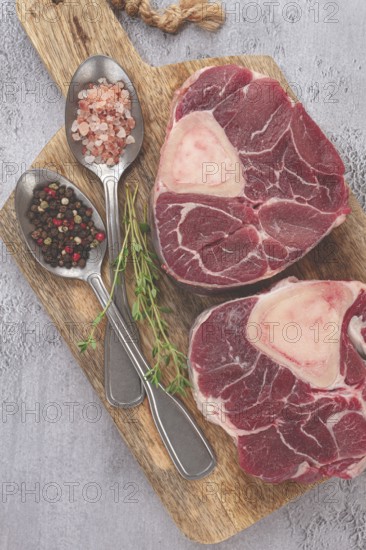 Freshly sliced beef legs, two ossobuco steaks, on a wooden board, with spices and herbs, ready to