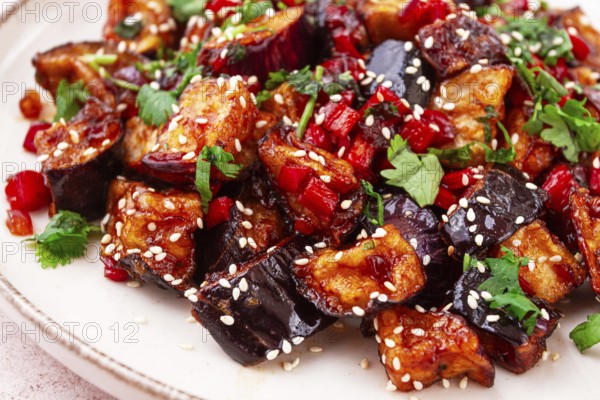Fried eggplant, Chinese style, in sweet and sour sauce, with pepper and sesame seeds. on a white