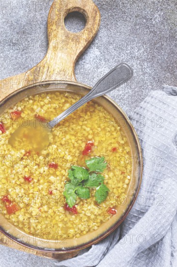 A nourishing bowl of lentil soup filled with grains and vibrant red pepper pieces sits on a