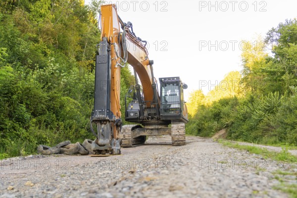 A large excavator stands on a dirt road in a wooded area, Hermann Hessebahn construction site,