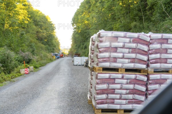 Stacked pallets of building materials line a gravel road in the forest, Hermann Hessebahn