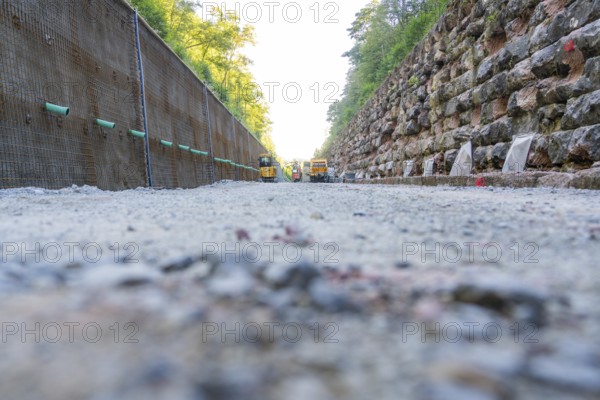 Gravel path between a concrete and a stone wall with construction machinery in the background,