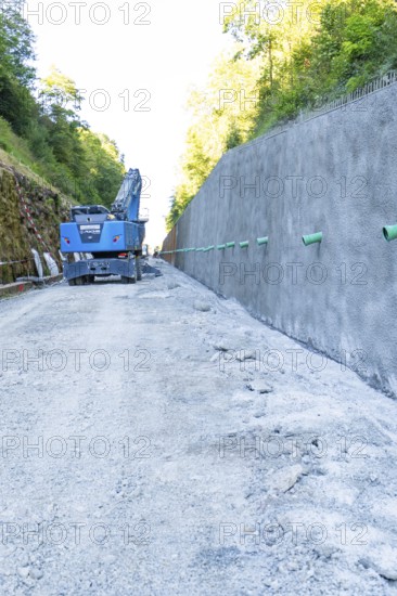 Construction site scene with blue crane next to a high concrete wall and gravel path, Hermann