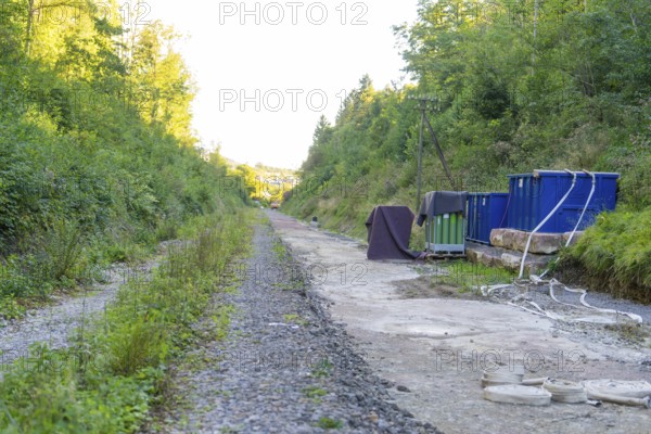 Gravel path with containers and cables in a wooded area along the track, Hermann Hessebahn