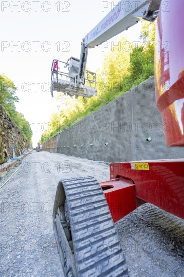 Red lifting platform on a gravel path in front of a concrete wall in the sunshine, Hermann