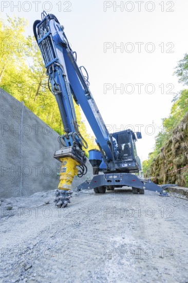 Blue crane with drill head on construction site on concrete wall, surrounded by nature, Hermann
