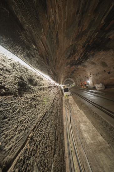 An illuminated tunnel with rails leading into the depths. The walls are made of stone and