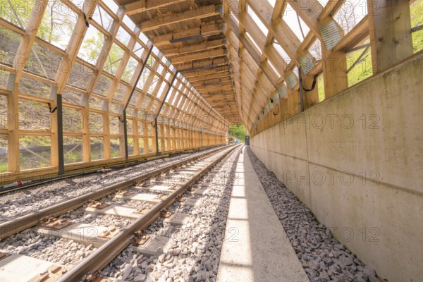 Light-flooded wooden tunnel with railway tracks and concrete path, surrounded by nature,