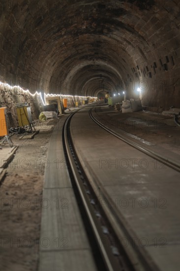 An illuminated railway tunnel, partly construction site with visible brick walls, construction of