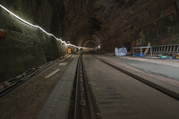 A tunnel with stone walls and railway tracks, illuminated and with building accessories,