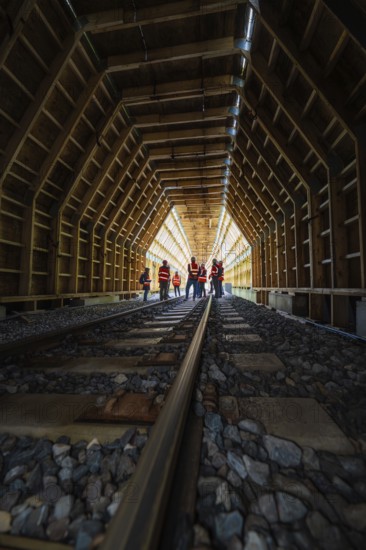 Group of employees in an illuminated wooden tunnel on railway tracks, construction of the Hermann