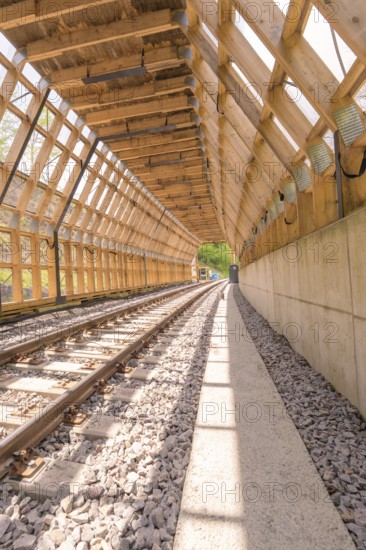 Wooden tunnel structure over railway tracks, bright sunlight floods the room, construction of the