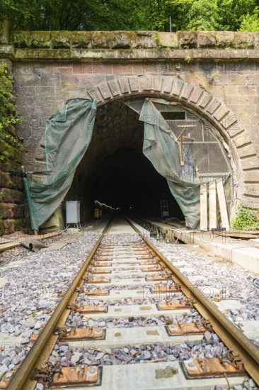 Railway tunnel with rails and stone wall, surrounded by green plants, renovation work in progress,