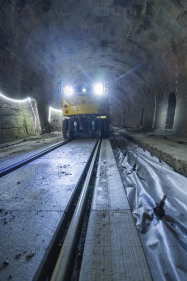 A yellow vehicle with bright lights stands in the tunnel, the rails are visible, construction of