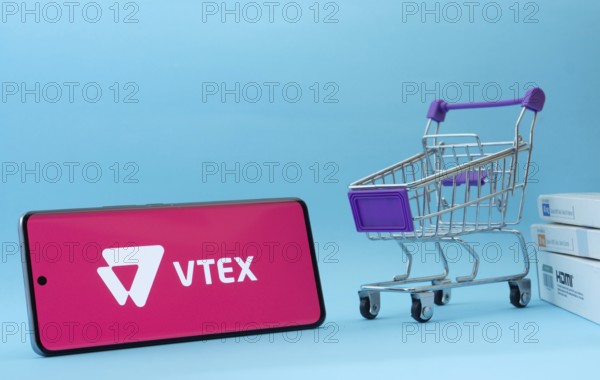Dhaka, Bangladesh- 03 July 2025: Smartphone with VTEX logo next to a small shopping cart and boxes