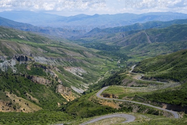 Winding roads lead down through a green valley into mountainous terrain under a clear sky, view