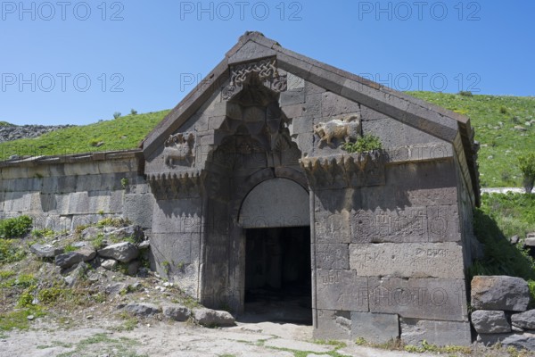 An old stone building with reliefs and a large entrance surrounded by green hills, Selim