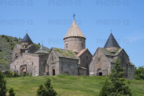 An old monastery with several towers and cross-decorated roofs on a green hill under a clear blue