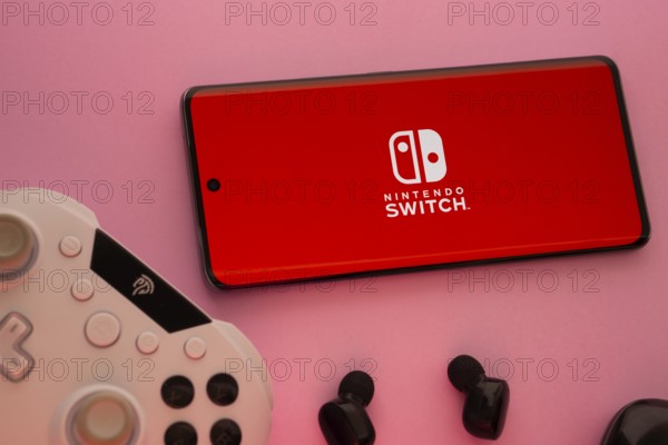 Dhaka, Bangladesh- 15 July 2025: Smartphone with nintendo switch logo, game controller, and earbuds