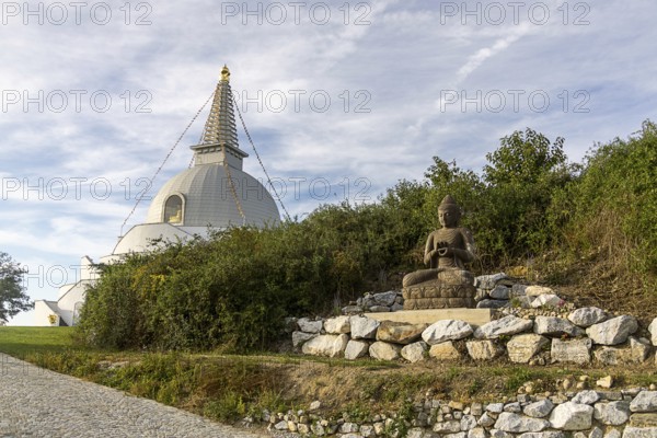 Buddha statue sitting on stones next to a pagoda in a green landscape, Stupa am Wagram Grafenwörth