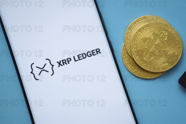 Dhaka, Bangladesh- 26 Aug 2025: XRP Ledger logo on smartphone screen near Bitcoin coin and QR code