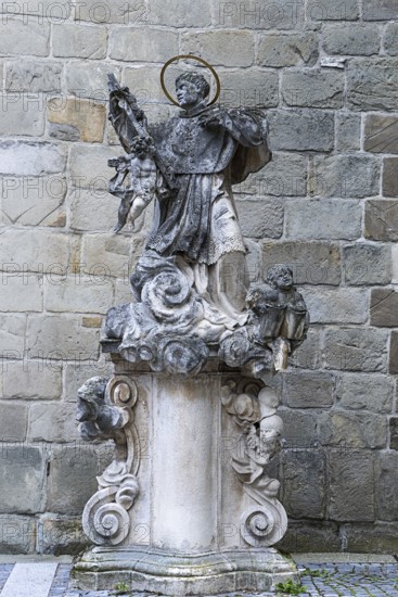 Stone statue of a saint on an ornate pedestal, baroque details in front of a stone wall, parish