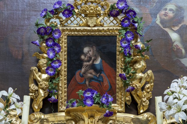 Medieval religious painting in a richly decorated golden frame with flowers and angels,